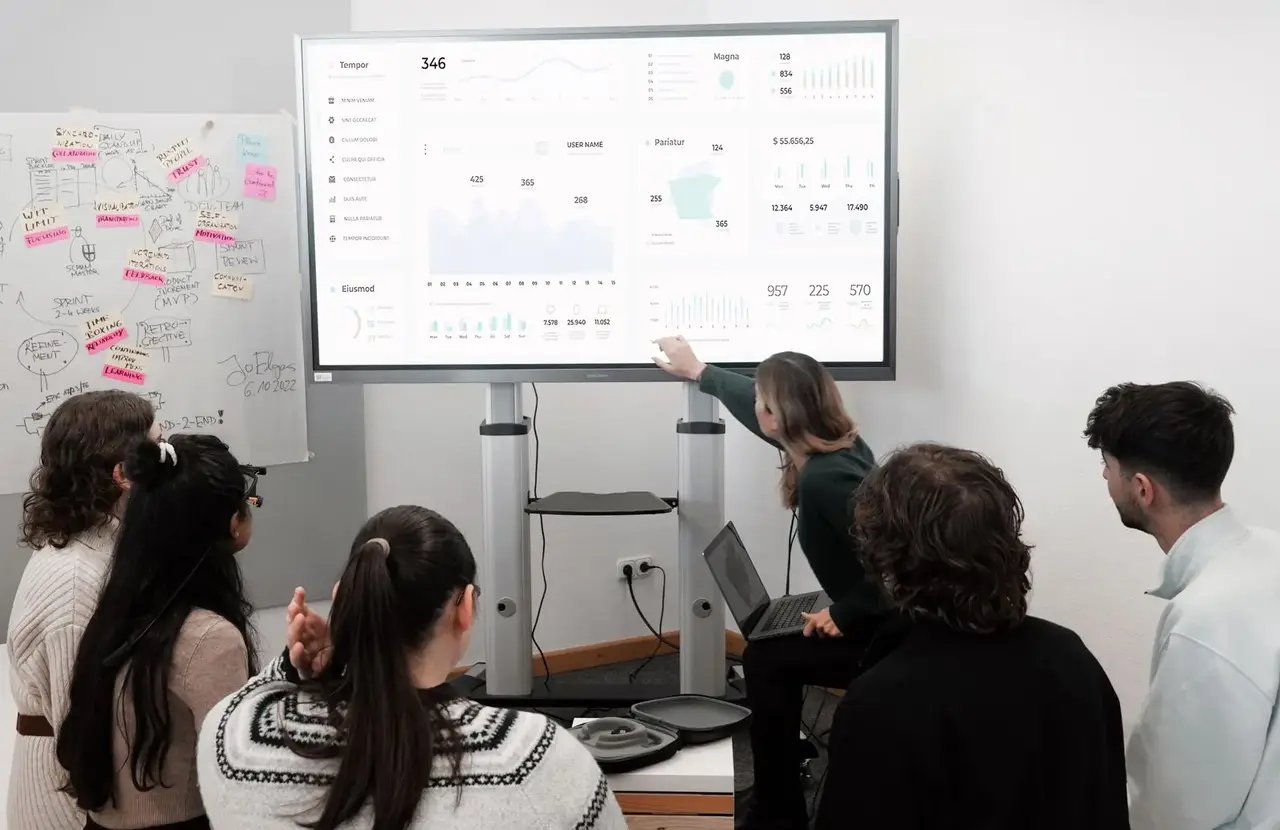 A group standing in front of a large screen showing a dashboard of charts.