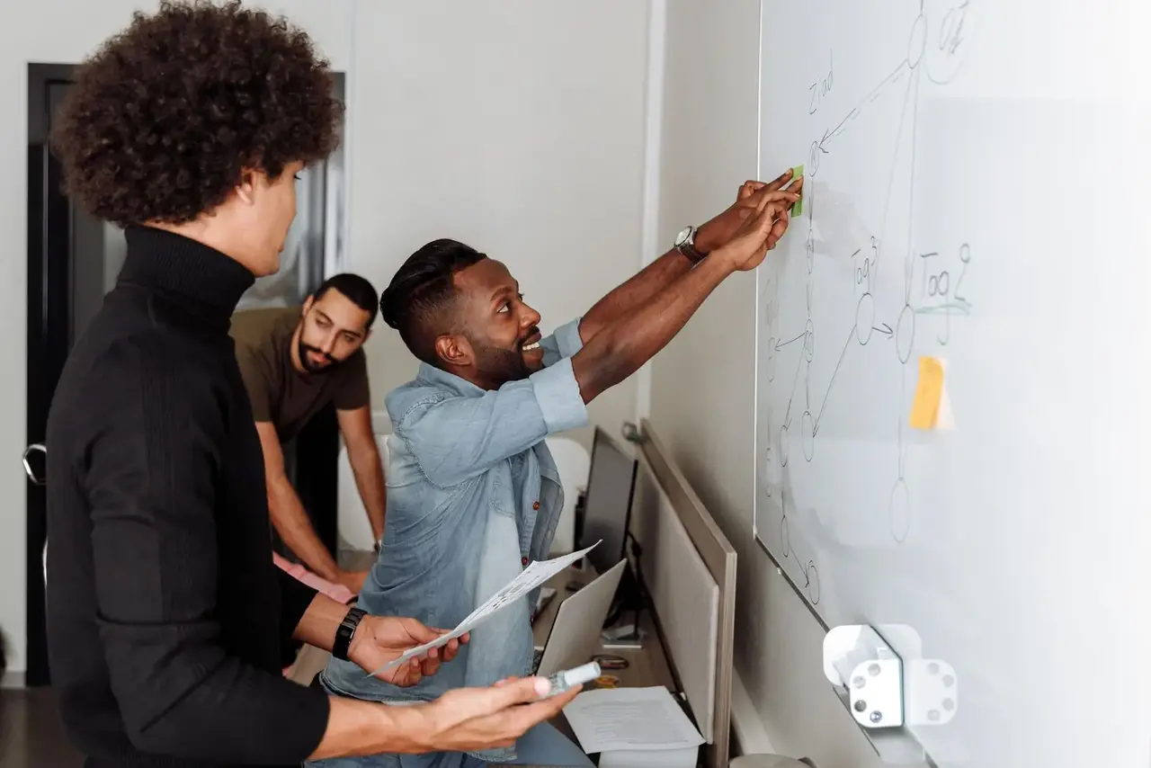 Colleagues at a whiteboard, one drawing a diagram while the others watch.