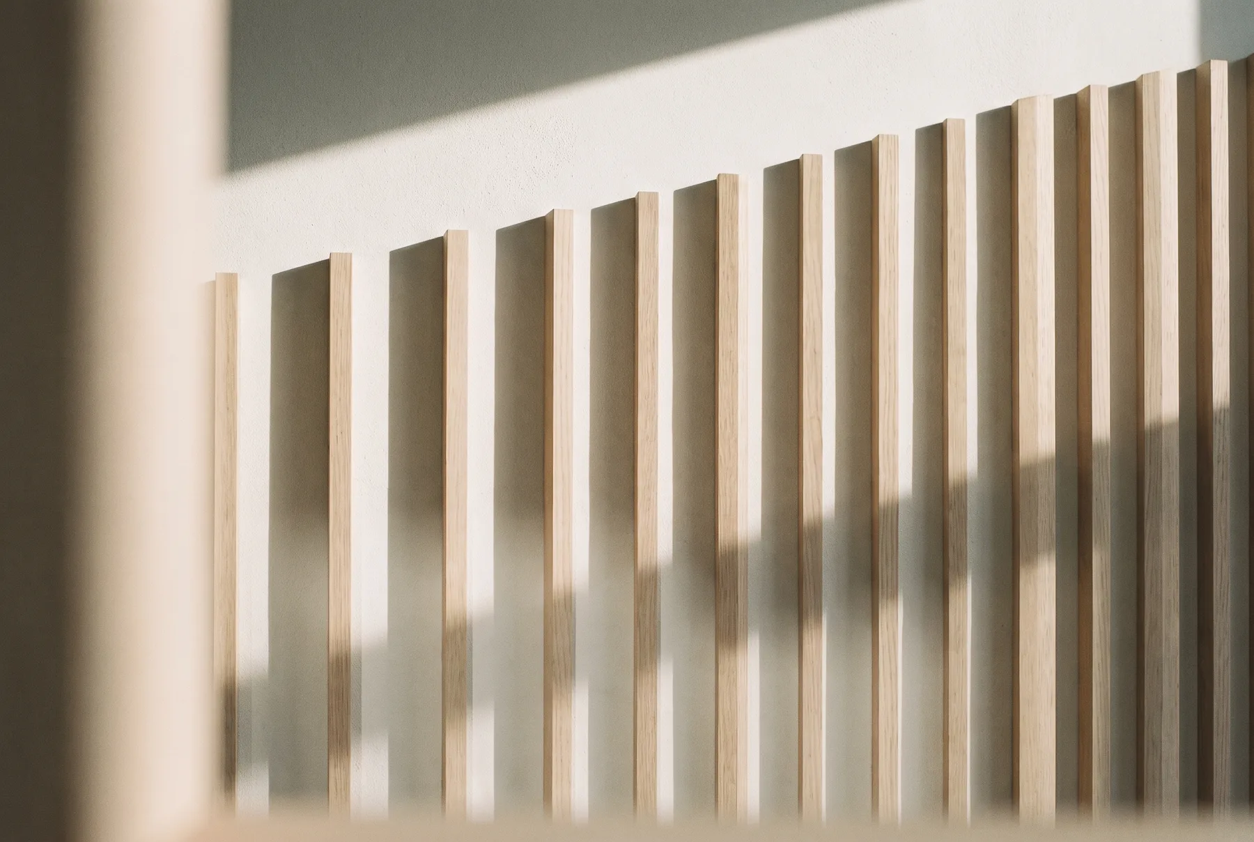 A wall of vertical timber battens in raking daylight, each throwing its own shadow.