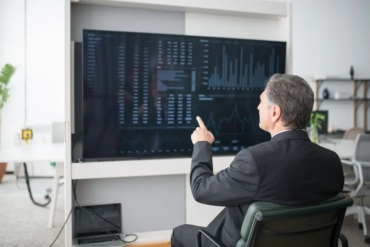 A man in a suit studying a wall-sized screen of charts and figures.